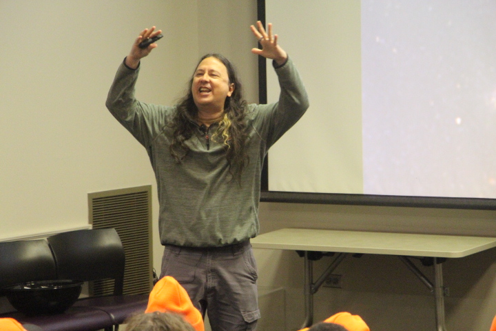 Mikhael speaking, arms raised